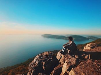 Man sitting on cliff against sea during sunset