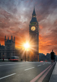 Blurred motion of vehicles on road by big ben against sky during sunset