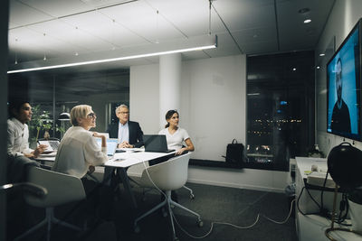Colleagues looking at businessman during video conference meeting at night in office