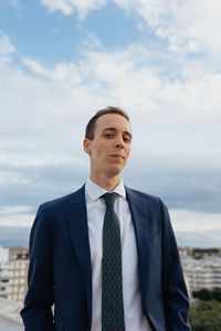 Young businessman in a suit and tie looking at camera and smiling while standing with a cloudy sky