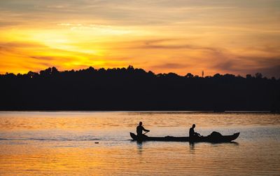 Silhouette people on boat against sky during sunset