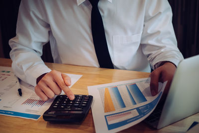 Midsection of businessman analyzing paperwork on table