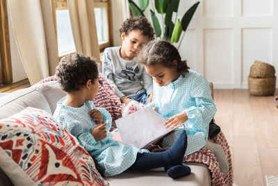 Siblings with book on sofa at home