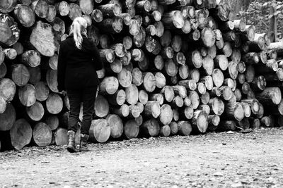 Rear view of woman standing by stacked logs