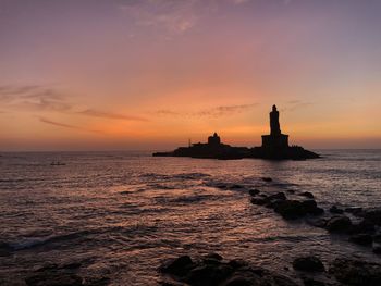 Silhouette of lighthouse in sea during sunset