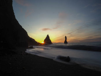 Silhouette rock formation on beach against sky during sunset