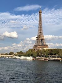 Eiffel tower by river against cloudy sky in city