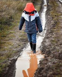 Full length of boy walking on muddy pathway amidst field