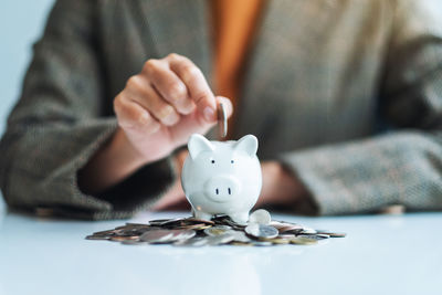 Midsection of man putting coin in piggy bank on table