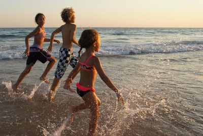 Rear view of siblings standing at beach during sunset