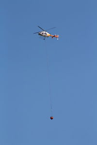 Low angle view of rope hanging from helicopter against clear blue sky