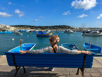 Rear view of woman sitting on bench against sky