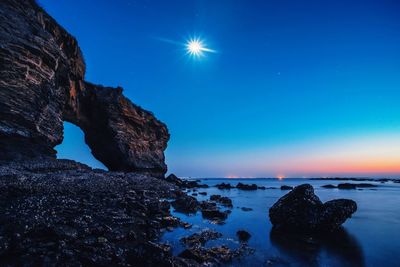 Moon shining over rock formations in blue sea