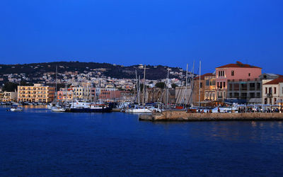 Sailboats moored in sea by town against clear blue sky