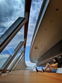 Rear view of woman sitting on railing against sky