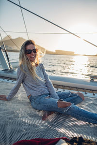 Portrait of smiling young woman sitting on boat against sky during sunset