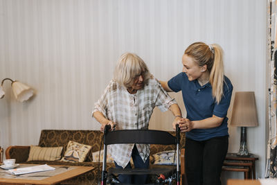 Smiling female care assistant helping senior woman using walker at home