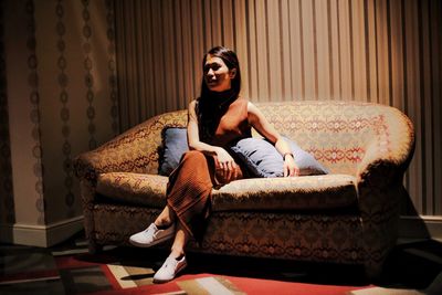 Full length of young woman sitting on sofa in room