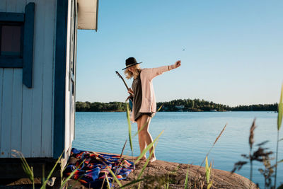 Woman stood smiling whilst holding her guitar at the beach