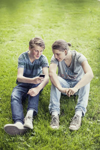 Young male friends using mobile phone on grass at park