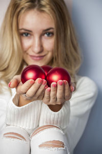 Portrait of smiling woman holding christmas ornaments while sitting against wall