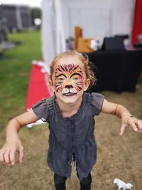 Portrait of cute smiling girl with tiger face paint standing on field