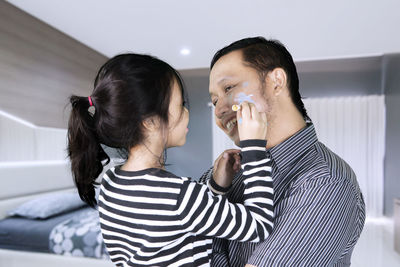 Daughter drawing with chalk on father cheek at home