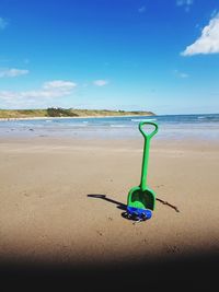 Green toy on beach against blue sky