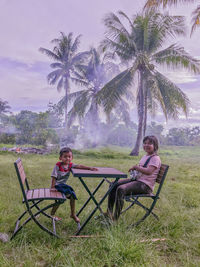 Full length of sibling sitting on chair at table outdoors