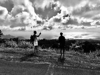 Rear view of men standing on field against sky