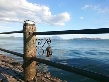 Old gas light hanging by pier over sea against sky