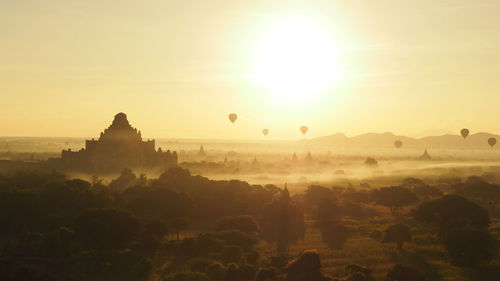 Hot air balloons over silhouette temples against sky during sunrise