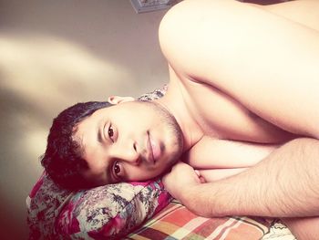 Portrait of shirtless young man lying on bed at home