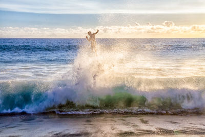 Waves splashing on shore against sky during sunset