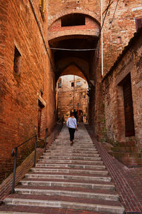 Rear view of woman walking on alley amidst buildings