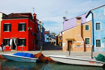 Boats moored on canal by buildings in city against sky