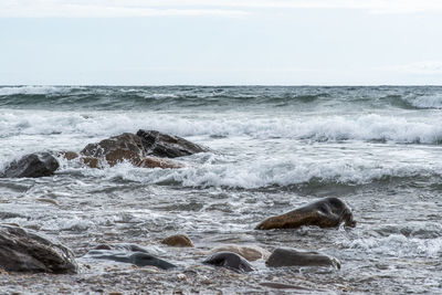 Scenic view of sea waves crashing into rocks against sky