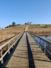 View of wooden footbridge against clear blue sky