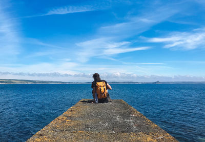 Rear view of woman sitting on sea against sky