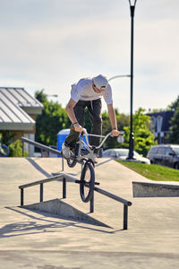 Rider riding bmx bike on railing against sky at skateboard park during sunny day