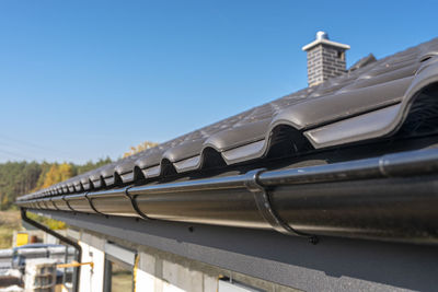 A metal, black gutter on a roof covered with ceramic tiles. close up shot.