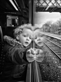 Portrait of cute girl pointing while leaning on window in train