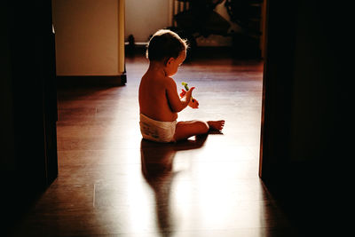 Cute baby girl holding toothbrush while sitting on hardwood floor