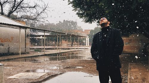 Man standing by wet tree against sky