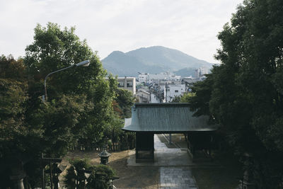 House and trees by buildings against sky