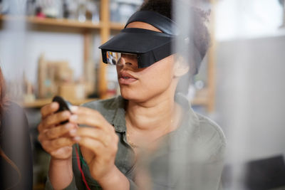 Female technician looking at electrical component through loupe in workshop