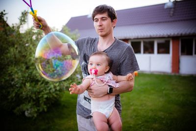 Man holding daughter by bubble in yard