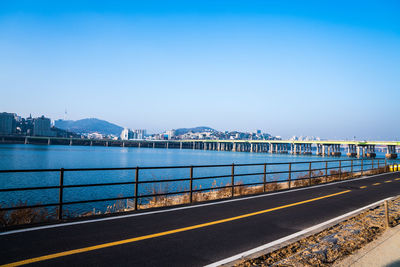 Road by sea against clear blue sky