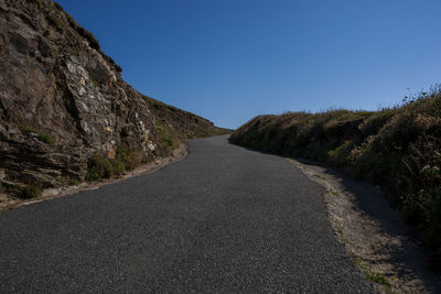 Empty road amidst trees against clear blue sky
