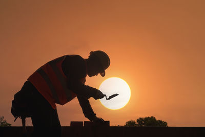 Low angle view of silhouette man standing against orange sky